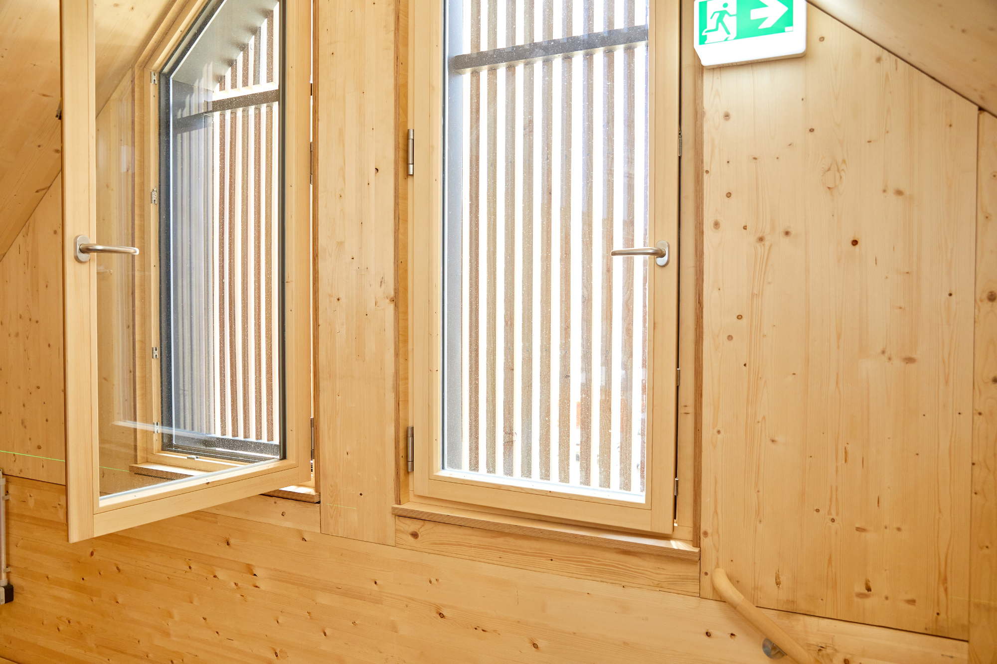 Die Außenwände, Innenwände und das Dach bestehen aus großformatigen Plattenelementen aus Fichte. Durch die Fenster hinter der Lattenschalung kommt Tageslicht in die Restaurierungswerkstatt im Dachgeschoss. Die Außenwände, Innenwände und das Dach bestehen aus großformatigen Plattenelementen aus Fichte. Durch die Fenster hinter der Lattenschalung kommt Tageslicht in die Restaurierungswerkstatt im Dachgeschoss.