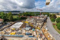 Ein Blick über die Baustelle nach Westen zeigt im Vordergrund das fertige Untergeschoss des Parkdeck- und Kantinengebäudes, dann der Tiefgaragen-Verbindungsbau (Schalarbeiten) und dahinter das künftige Hauptgebäude des Neubaukomplexes.