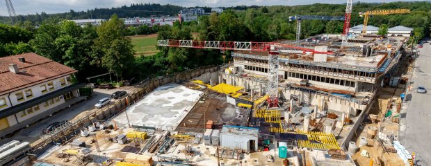 Ein Blick über die Baustelle nach Westen zeigt im Vordergrund das fertige Untergeschoss des Parkdeck- und Kantinengebäudes, anschließend der Tiefgaragen-Verbindungsbau (Schalarbeiten) und dahinter das künftige Hauptgebäude des Neubaukomplexes.