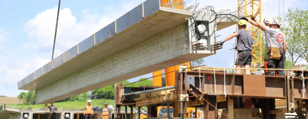 Die neue Brücke über die Mitternacher Ohe bei Eberhardsreuth wächst. Diese Woche werden die Beton-Fertigteile für den Brückenüberbau eingehoben. Die tonnenschweren Betonträger in Position zu bringen erfordert höchste Präzision – und eine logistische Meisterleistung.
